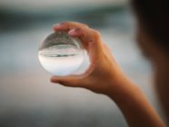 Крупный план руки ребенка, держащего стеклянный шар на фоне размытых волн — стоковое фото