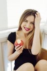 Giovane donna sorridente che tiene mela sulla sedia e guarda la fotocamera — Foto stock