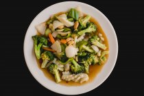 Зверху приготований смачний гарячий суп з кальмарами та корисними овочами, такими як брокколі, морква, цибуля, огірок на чорному тлі — стокове фото