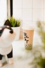 Tasty milk bubble tea with tapioca pearls in plastic cup on table near potted plants in traditional Taiwanese cafe — Stock Photo