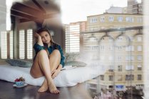 Молодая женщина сидит на кровати и смотрит через окно — стоковое фото