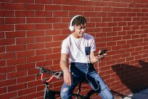Junger glücklicher schwarzer Mann hört Musik mit Smartphone auf dem Fahrrad — Stockfoto