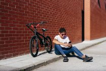 Joven hombre negro feliz navegación smartphone en bicicleta - foto de stock