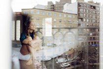 Jovem mulher sentada na cama e olhando pela janela — Fotografia de Stock