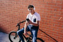 Joven hombre negro feliz escuchando música con smartphone en bicicleta - foto de stock
