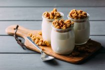 Vasos de leche fría y deliciosa granola sobre tabla de madera sobre mesa gris - foto de stock