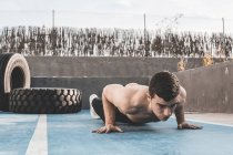 Musclé jeune gars faire des pompes tout en exerçant sur le sol en béton du terrain de sport sur la rue de la ville — Photo de stock