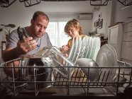 Злий дорослий чоловік і хлопчик з інструментами під час ремонту посудомийної машини на кухні — стокове фото
