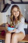 Jovem mulher comendo morangos na cozinha — Fotografia de Stock