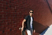 Молодой черный человек с длинной доской опираясь на стену — стоковое фото