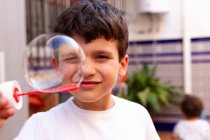 Little boy in white T-shirt playing soap bubbles while standing on terrace at home — Stock Photo