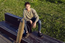 Jovem negro sentado no banco com skate — Fotografia de Stock