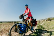 Леди в спортивной одежде и шлеме катается на велосипеде по каменистой дорожке, путешествуя по лесу в солнечный день в сельской местности — стоковое фото