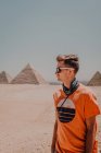Selbstbewusste männliche Reisende mit Sonnenbrille, die wegschauen, während sie in der Wüste vor den berühmten Großen Pyramiden in Kairo stehen, Ägypten — Stockfoto