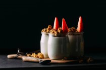 Bicchieri di latte freddo gustoso e delizioso muesli con fragole su tavola di legno su sfondo nero — Foto stock