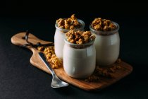 Glasses of cold tasty milk and delicious granola on wooden board on black background — Stock Photo