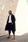 Alla moda giovane afroamericano maschio in abito elegante in posa sulla strada vicino muro grungy — Foto stock