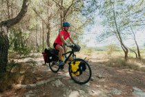 Lady in sportswear and helmet riding bike on stony path while traveling through forest on sunny day in countryside — Stock Photo