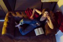 Молодая сексуальная женщина сидит на диване с яблоком и книгой — стоковое фото