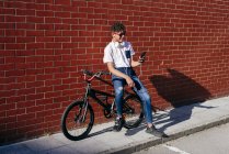 Молодой счастливый черный мужчина просматривает смартфон на велосипеде — стоковое фото