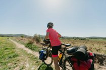 Lady in abbigliamento sportivo e casco in bicicletta sul sentiero pietroso mentre viaggia attraverso la foresta nella giornata di sole in campagna — Foto stock