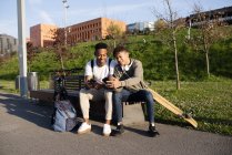 Young black men sitting on bench with smartphone — Stock Photo