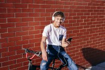 Молодий щасливий чорний чоловік слухає музику зі смартфоном на велосипеді — стокове фото
