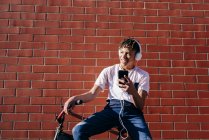 Молодой счастливый черный мужчина слушает музыку со смартфоном на велосипеде — стоковое фото