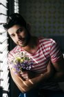 Young alone male in casual clothes sitting on chair with bouquet of flowers and looking at camera — Stock Photo
