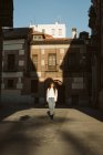 Модна молода жінка в повсякденному вбранні, що йде на тротуарі старого міста в сонячний день — стокове фото