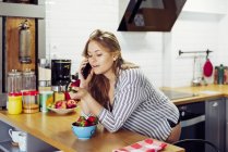 Jovem mulher navegando smartphone na cozinha — Fotografia de Stock