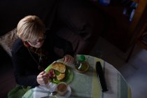 Зверху літня жінка п'є каву зі скла за сніданком, сидячи за столом — стокове фото