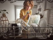 Garçon avec des outils tout en réparant le lave-vaisselle dans la cuisine — Photo de stock