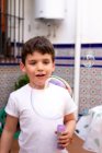 Pequeño niño en camiseta blanca jugando burbujas de jabón mientras está de pie en la terraza en casa - foto de stock