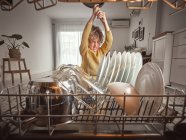 Annoyed little boy yelling while putting frying pan into open dishwasher in kitchen — Stock Photo