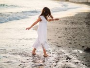 Menina em vestido branco andando na água na praia — Fotografia de Stock