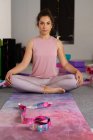 Serious young brunette in sportswear sitting in yoga position and looking at camera — Stock Photo