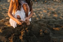 Крупный план женщины в белом платье, играющей с песком на пляже в солнечном свете — стоковое фото