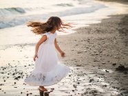 Menina em vestido branco jogando na praia ao pôr do sol — Fotografia de Stock