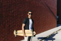 Young black man with long board standing near wall — Stock Photo