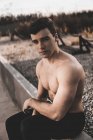 Muscoloso ragazzo senza maglietta guardando la fotocamera mentre appoggiato sul muro di cemento durante l'allenamento sulla strada della città — Foto stock