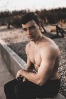 Muscular shirtless guy looking at camera while leaning on cement wall during training on city street — Stock Photo