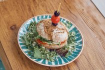 Смачний вегетаріанський бутерброд з помідорами, цибулею, салатом, оливками та вишневим помідором на яскравій тарілці на дерев'яному столі в ресторані — стокове фото