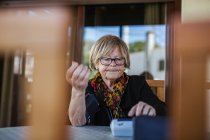 Seniorin misst mit Tensiometer Blutdruck, während sie zu Hause am Tisch sitzt — Stockfoto