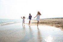 Happy and smiling children in casual wear running barefoot along seashore on sandy beach in summer sunny day — Stock Photo