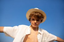 De acima mencionado menino atraente em chapéu e camisa desabotoada de pé com as mãos abertas — Fotografia de Stock