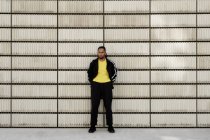 Молодой афроамериканец в модной спортивной одежде смотрит в камеру, стоя возле цементных блоков на городской улице — стоковое фото