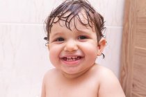 Очаровательный ребенок смотрит на камеру с мокрыми волосами, сидя на полотенце в ванной комнате после душа — стоковое фото