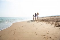 Щасливі і усміхнені діти в повсякденному вбранні бігають босоніж уздовж берега моря на піщаному пляжі в літній сонячний день — стокове фото