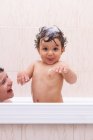 Vista laterale del ragazzo che soffia bolla in faccia al bambino carino mentre si fa il bagno insieme — Foto stock
